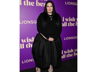 Lena Dunham at a promotional event, standing in front of a purple backdrop featuring text related to a film title.