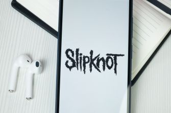 Image of a smartphone displaying the Slipknot logo on a white background, with a notebook and earphones nearby.