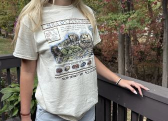 A person wearing a vintage Monterey Bay Aquarium T-shirt featuring a sea otter design.