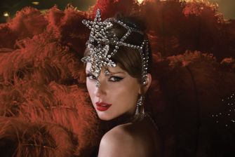 A glamorous individual wearing a jeweled headpiece and striking red lipstick, with vibrant feathered decor in the background.