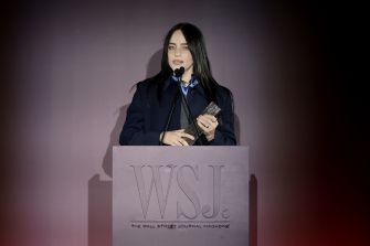 Billie Eilish speaks at an event, holding an award while standing at a podium with the WSJ logo.