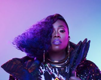 Missy Elliott posing with vibrant lighting and styled hair, wearing bold fashion accessories.