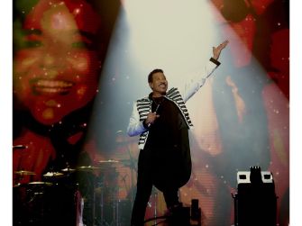 Lionel Richie performing onstage with vibrant lighting and visuals behind him during his concert.