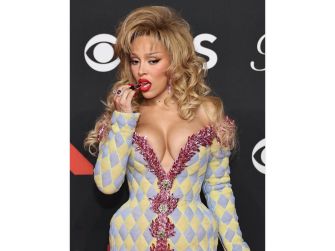 Doja Cat posing in a glamorous outfit at an event, looking thoughtful while holding a piece of candy.