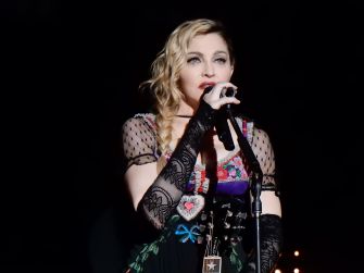A singer performing on stage with a microphone, wearing a colorful dress and gloves.