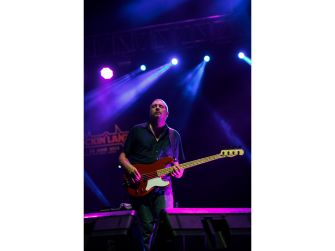Bassist performing on stage with a guitar, illuminated by colorful stage lights.