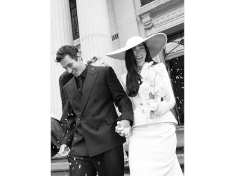 Dua Lipa and Callum Turner smile as they exit a venue, holding hands and surrounded by confetti on their wedding day in London.