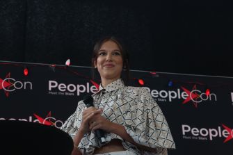 A young woman holding a microphone and smiling at an event with a "PeopleCon" backdrop.