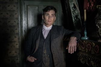 A character in a vintage setting, leaning against a wall, dressed in early 20th-century attire.