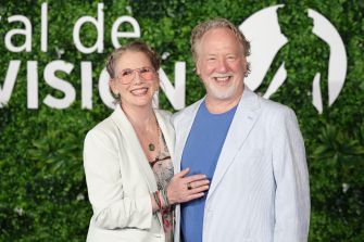 Melissa Gilbert and Timothy Busfield at a public event, smiling together in front of a greenery backdrop.