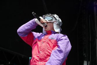 A performer singing into a microphone while wearing a colorful outfit and ski goggles on stage.