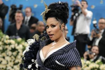 Nicki Minaj posing at a glamorous event with a floral background and photographers in the distance.