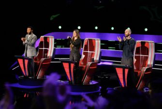 Three coaches on stage at a live taping of a singing competition, applauding.