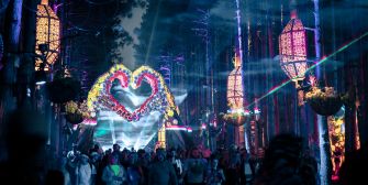 A vibrant scene from the Electric Forest Festival featuring illuminated decorations and festivalgoers amidst trees.
