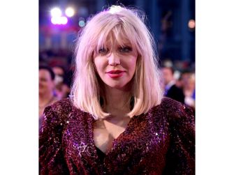 Courtney Love at an event, wearing a sparkling outfit and looking directly at the camera.