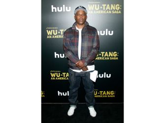 A man standing in front of a promotional backdrop for the Hulu series "Wu-Tang: An American Saga."