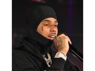 Rapper Pooh Shiesty performing on stage with a microphone, wearing a black outfit and beanie.