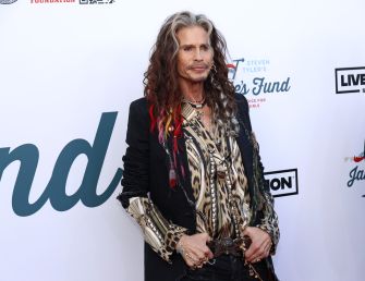 Steven Tyler posing at an event while wearing a patterned shirt and jacket.