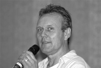 Anthony Head speaking into a microphone at an event.