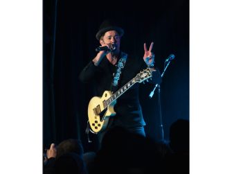 A musician performing on stage with a guitar, giving a peace sign to the audience.