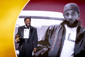 Kendrick Lamar accepting a Grammy Award with a backdrop featuring one of his images.
