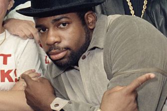 Image of Jam Master Jay, a key figure in hip-hop and founding member of Run-DMC, posing in a light-colored outfit and a black hat during a photo event.