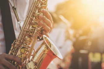 Close-up of a saxophone being held, with sunlight illuminating the scene, emphasizing the instrument's shine and details.