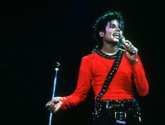 Michael Jackson performing live, wearing a red shirt and holding a microphone.