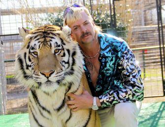 A man posing with a tiger, wearing a sequined jacket, at an animal park.