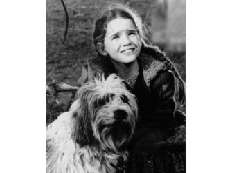 A young girl smiling beside a dog, in a serene outdoor setting, evoking a sense of nostalgia.