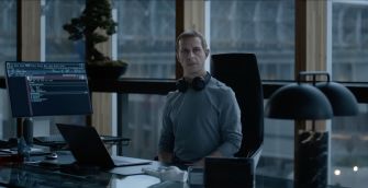 A character sitting at a desk with a computer and headphones in a modern office setting, looking contemplative.