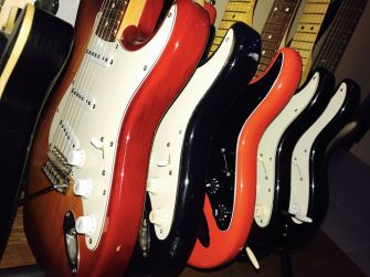 A collection of electric guitars with Stratocaster-style body shapes lined up in a display.