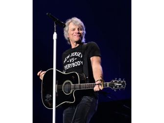 Jon Bon Jovi performing on stage with an acoustic guitar, wearing a black shirt.