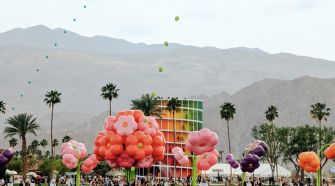 Colorful flower installations and a vibrant crowd at Coachella with mountains in the background.