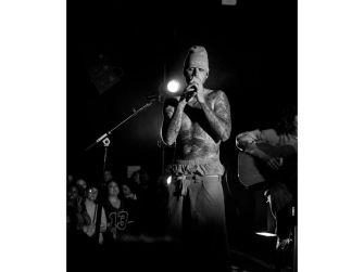 Justin Bieber performing at an intimate concert in Los Angeles, wearing a beanie and revealing tattoos, with an acoustic guitarist in the background.