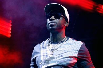 Rapper Gucci Mane performing on stage with dramatic lighting in the background.
