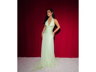 Becky G poses in an elegant green gown against a red backdrop.