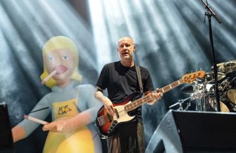 Sam Rivers performing on stage with a large inflatable figure in the background.