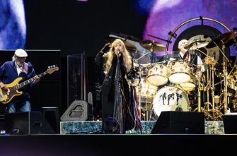 Fleetwood Mac performing live on stage, with band members playing instruments and singing.