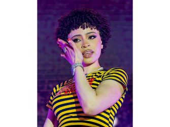 Image of Ice Spice performing on stage, wearing a striped shirt and featuring a curly hairstyle.