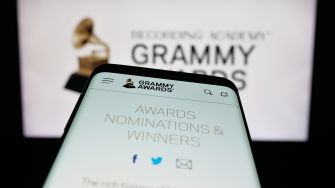 Close-up of a smartphone displaying the Grammy Awards website, with a Grammy trophy logo in the background.