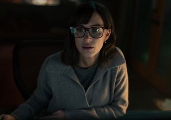 A woman with dark hair and glasses appears to be engaged in work on a computer, set in a dimly lit room.