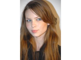 Photo of a young woman with long hair and blue eyes, looking towards the camera.
