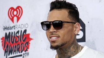 Chris Brown at a red carpet event, wearing sunglasses and a white shirt.