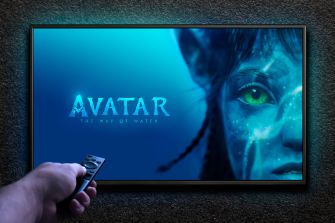 A person holding a remote in front of a television screen displaying promotional art for "Avatar: The Way of Water," featuring a close-up of the character Neytiri.
