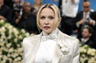 Madonna wearing a formal outfit at an event, surrounded by a floral backdrop and an audience.