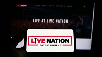 Logo of Live Nation Entertainment displayed on a smartphone in front of a blurred background featuring a Live Nation webpage.