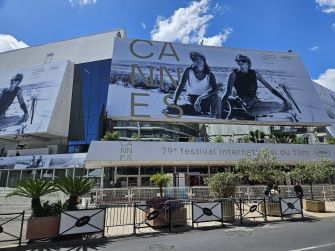 Exterior view of the Cannes Film Festival venue featuring large banners and palm trees.