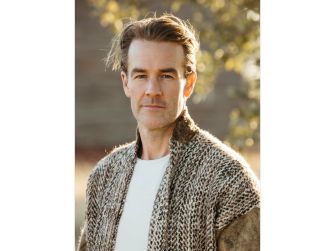 Image of a man with medium-length hair, wearing a textured knit sweater, posing outdoors with natural light.