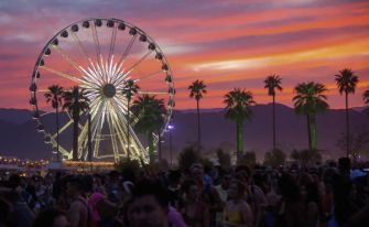 A vibrant sunset view of the Stagecoach Festival, featuring a illuminated Ferris wheel surrounded by palm trees and a crowd of attendees.